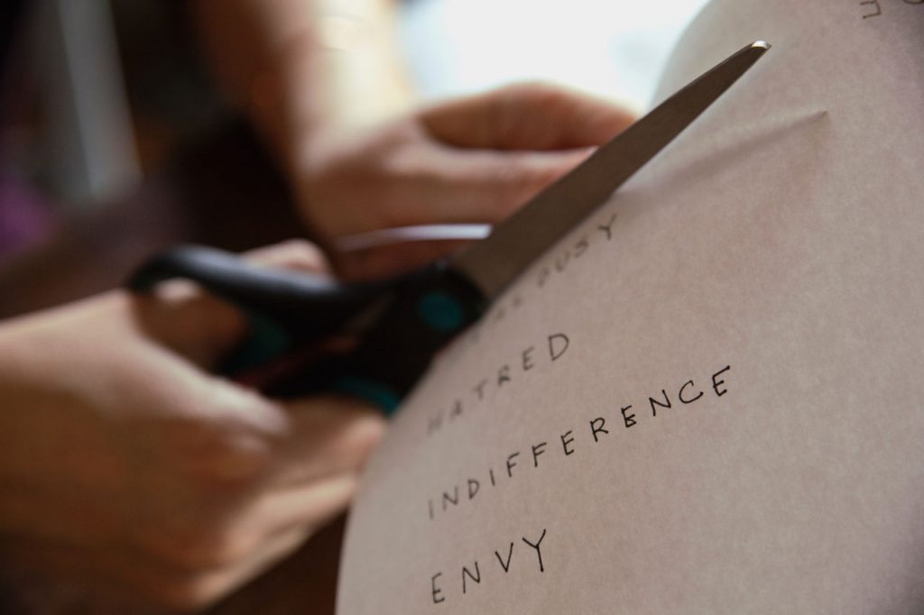 cutting paper that has words "hatred" and "envy", enemy