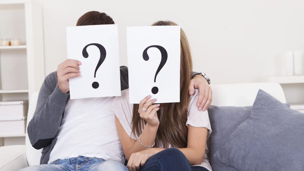 couple sitting and holding posters with question marks on them