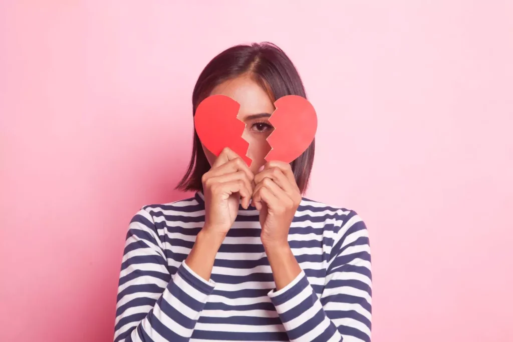 a symbol of a breakup, a woman is holding a paper heart ripped in two