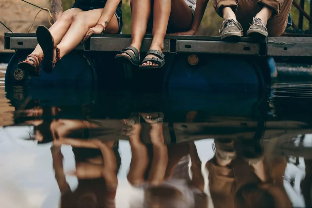 three friends sitting on a dock with their feet hanging over the edge above the water