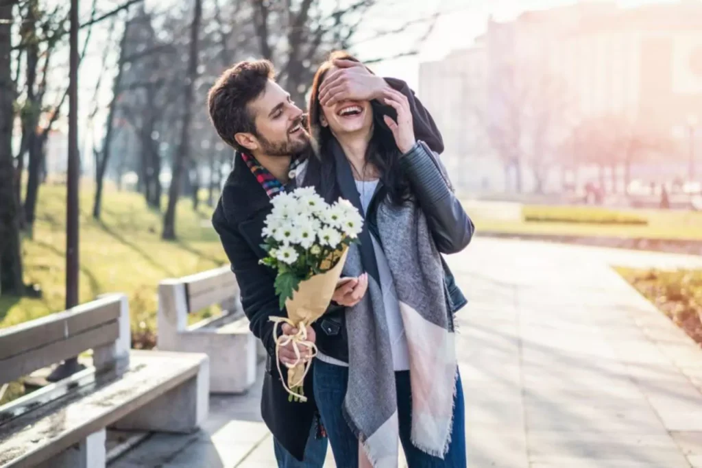 a man surprising a woman with white flowers like in a romantic comedy