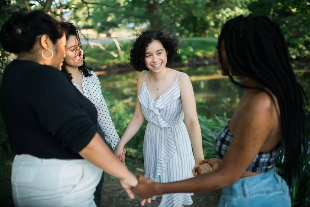 women standing in a circle, holding hands and smiling