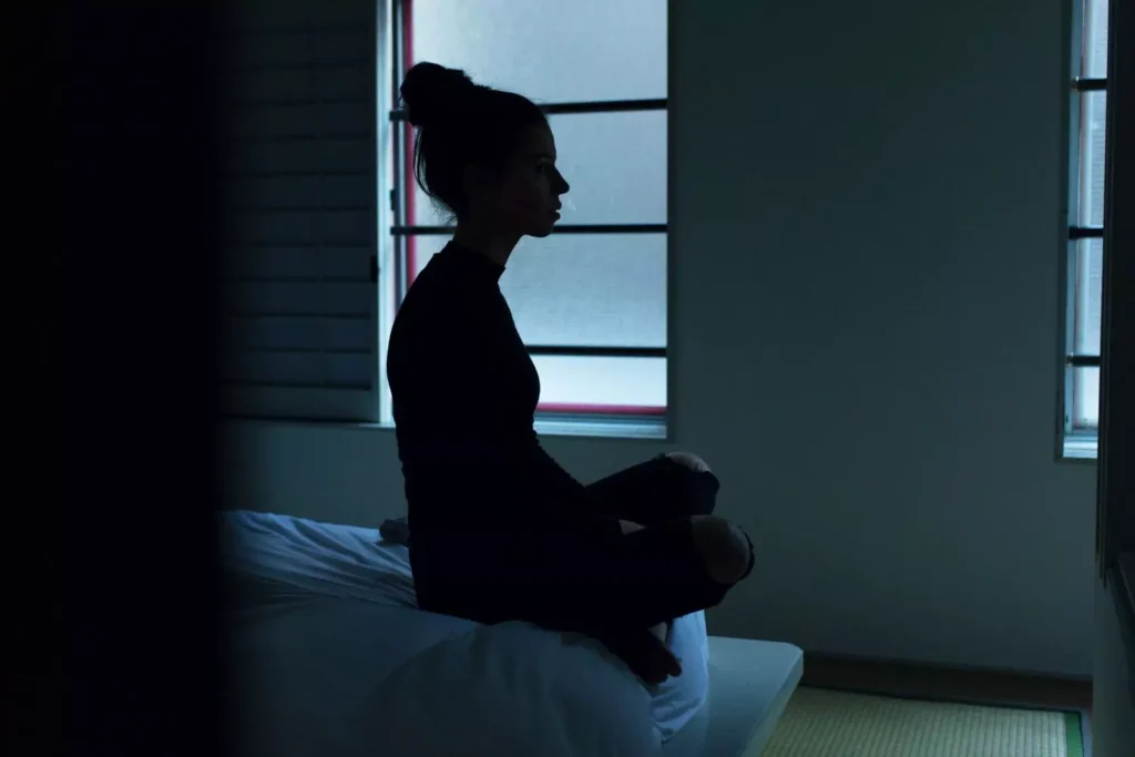 a woman with anxiety sitting on the edge of her bed in the dark